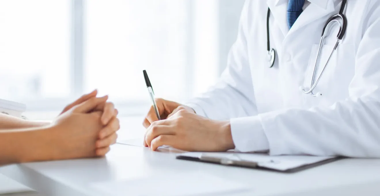 Un patient prend des notes pendant que le chirurgien explique un diagnostic sur un modèle d'anatomie.
